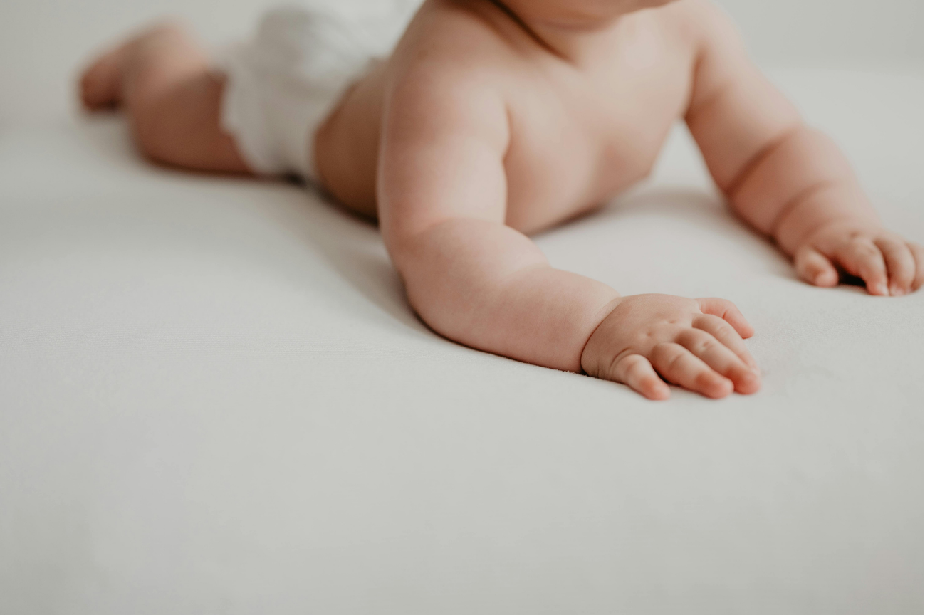 A baby lying on their front on a pale sheet, reaching forward